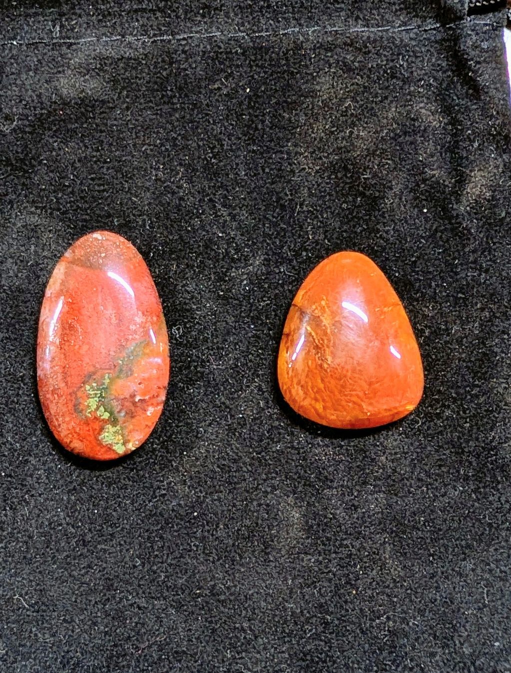 Two polished red-orange stones on black fabric.