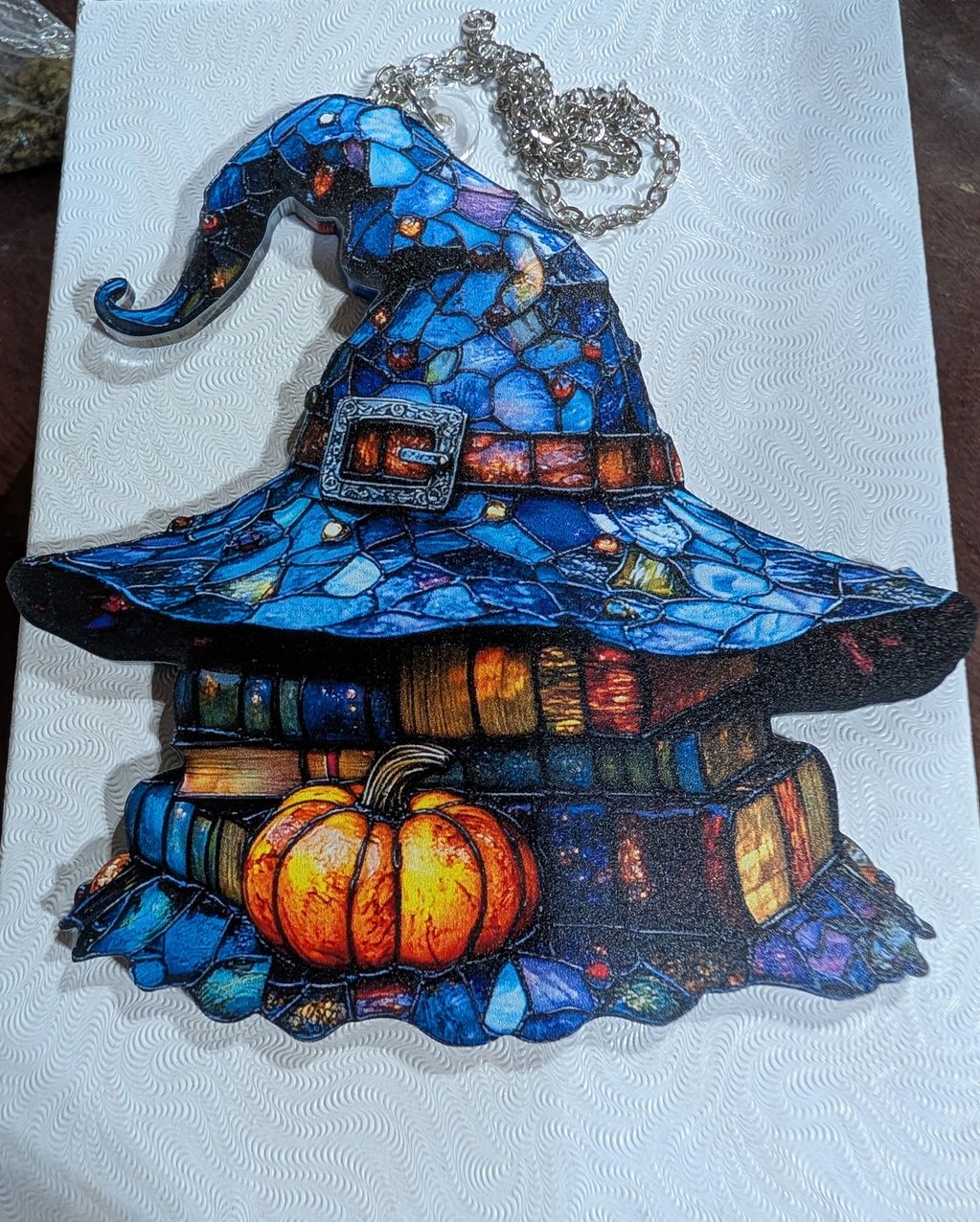 Pendant shaped like a witch's hat with books and pumpkin design.