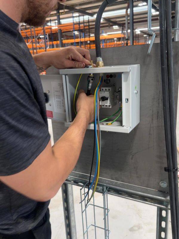Technician wiring an electrical control box in an industrial setting.