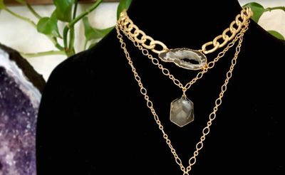 Layered gold chain necklaces with stone pendants on a black display bust.