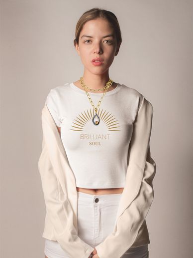 Woman in white crop top and blazer with gold necklace.