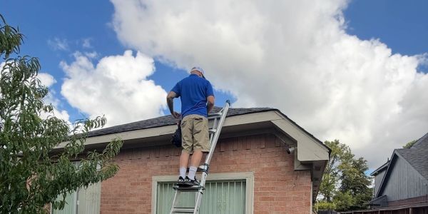 Man climbing ladder to roof of brick house on a sunny day.