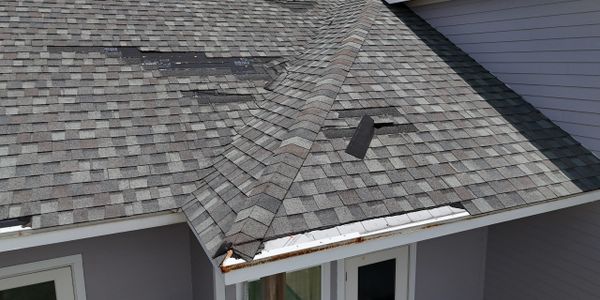 Damaged roof shingles with some missing and warped areas on a residential house.