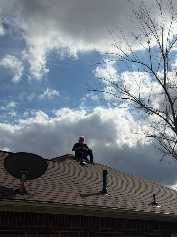 Person sitting on a rooftop under a cloudy sky.