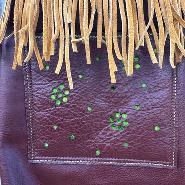 Close-up of leather with green stud embellishments and fringe.