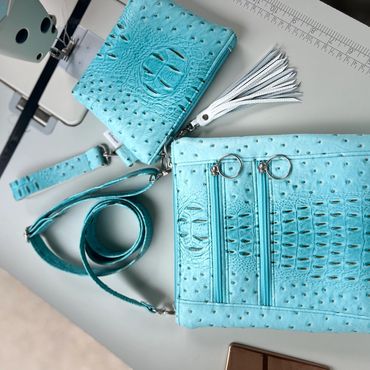 Turquoise crocodile-textured handbag and wallet on a table.