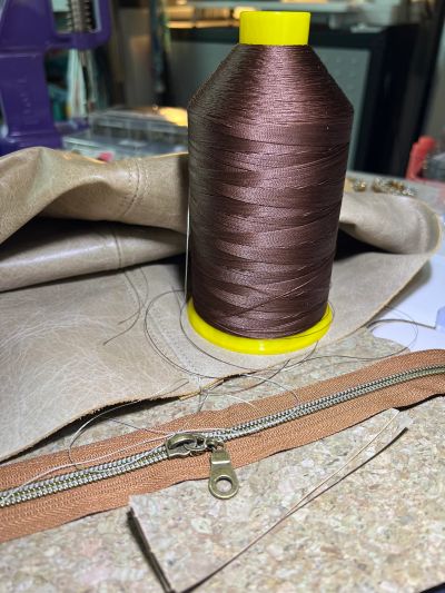 Brown sewing thread spool with zipper and beige fabric.
