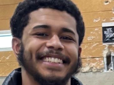 Young man smiling happily indoors with a brick wall background.