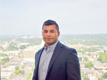Confident man in a suit standing with a cityscape background.