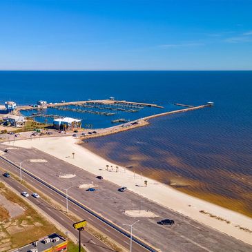 A coastal marina with a pier extending into calm blue waters under a clear sky.