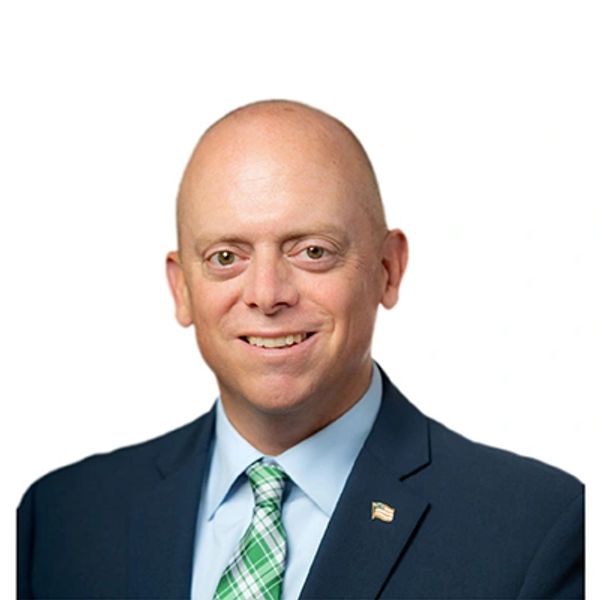 A smiling bald man in a suit with a green plaid tie.