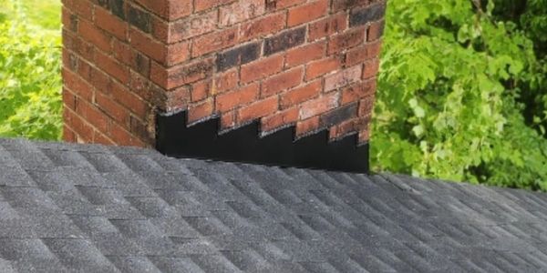 Brick chimney with new flashing on a shingled roof surrounded by greenery.