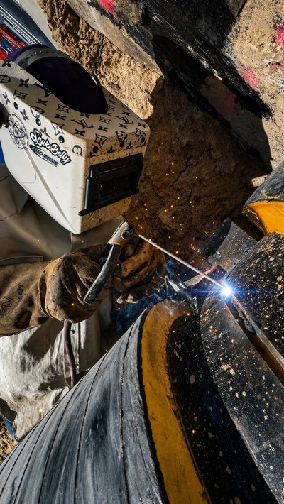 Worker welding a pipeline with protective gear.