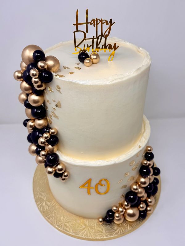 Elegant two-tier birthday cake with black and gold decorations.