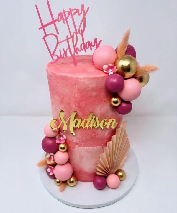 Pink birthday cake with decorations and the name Madison.