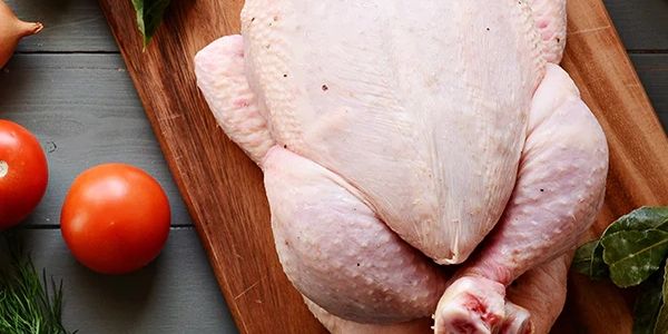 Raw whole chicken on a wooden cutting board.