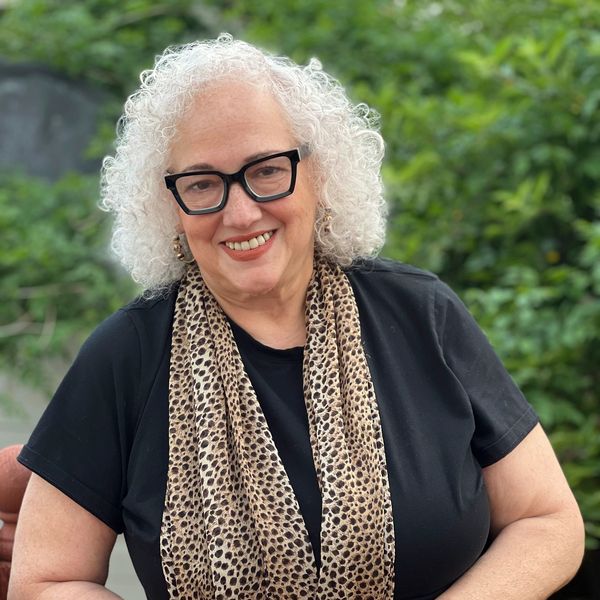 Smiling woman with curly white hair and glasses.