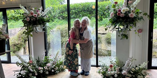 Two women smiling and hugging in a flower-decorated room.