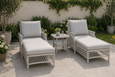 Two cushioned lounge chairs with a small table in a sunny garden patio.