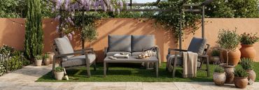 Cozy outdoor seating area with cushioned chairs and a coffee table under a pergola with hanging plants.