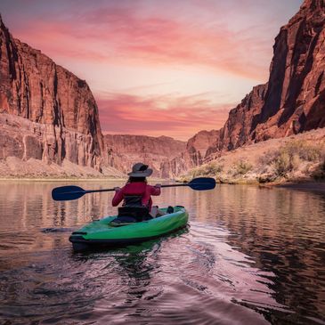 A person kayaking in a river surrounded by canyon cliffs at sunset.