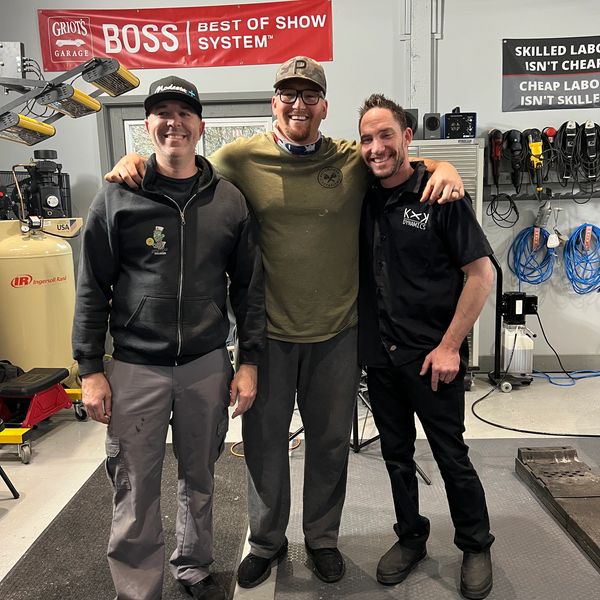 Three men smiling together in a workshop.