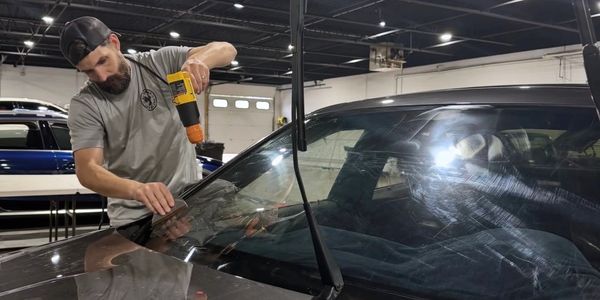 Man using drill on car windshield.