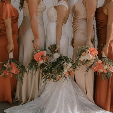 Bridesmaids and bride holding floral bouquets in elegant dresses.