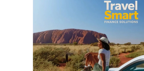 Woman in hat sitting on a car hood admiring a large red rock formation under a clear sky.