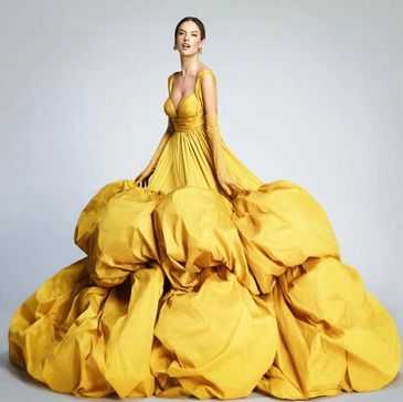 A woman in an extravagant yellow ball gown with voluminous fabric details.