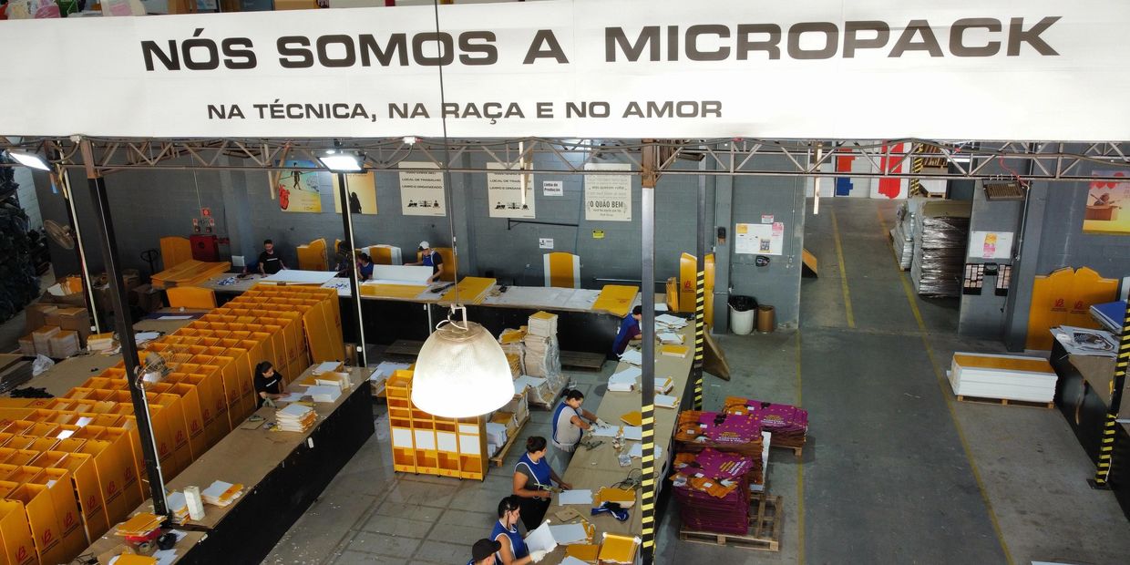 Fábrica da Micropack com trabalhadores organizando embalagens amarelas.