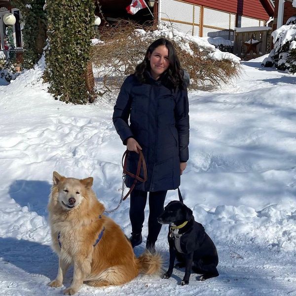 Woman in winter coat with two dogs on snowy path.