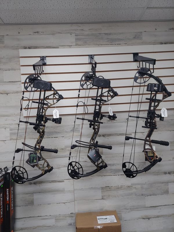 Three compound bows hanging on display hooks.