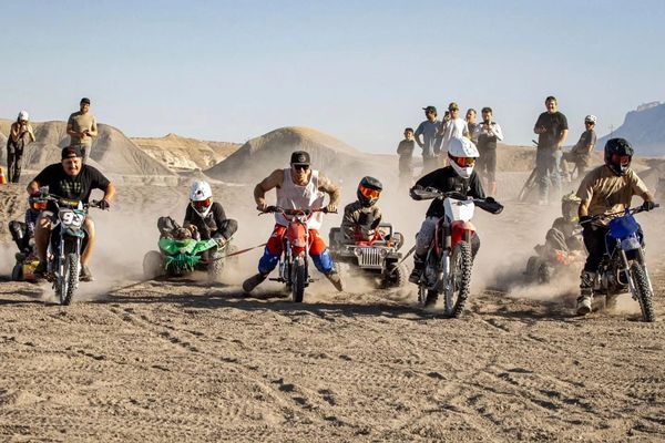 Group riding dirt bikes and mini vehicles on a dusty desert track.