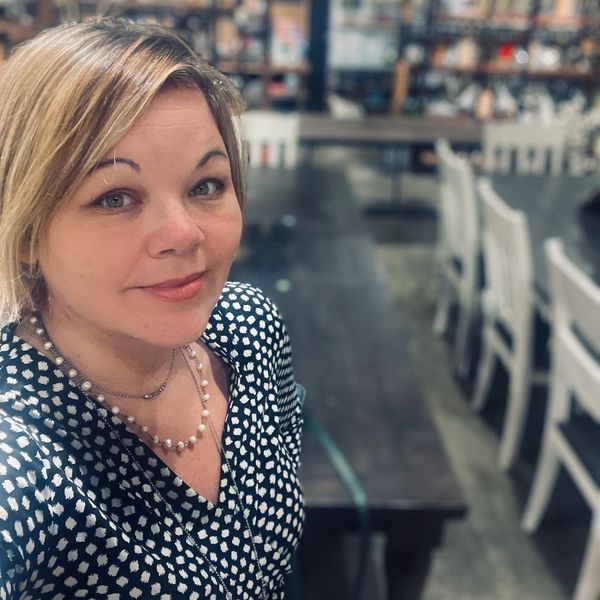 Woman in black and white patterned blouse taking a selfie indoors.