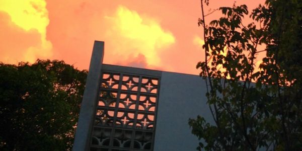 Atardecer naranja detrás de una estructura moderna con árboles.