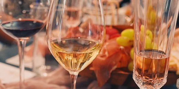 Various types of wine glasses with drinks and a food platter in the background.