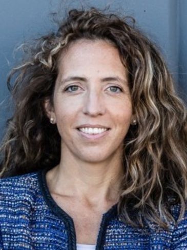 Smiling woman with curly hair and blue jacket.