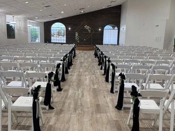 Indoor wedding ceremony setup with white chairs and black decorations.
