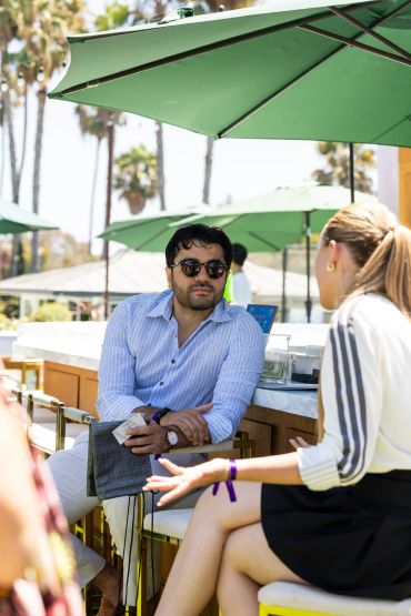 Two people having a conversation outdoors under green umbrellas.