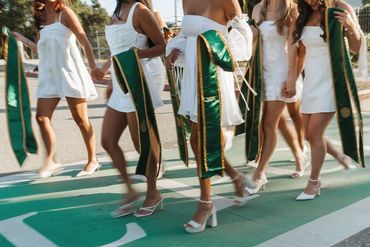 Group of graduates walking with green and gold sashes.