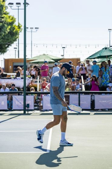Man playing tennis on an outdoor court with audience.