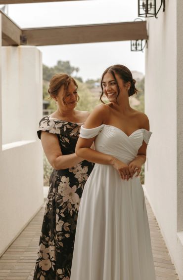 Bride smiling as woman helps with dress.