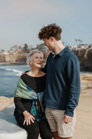 Elderly woman and young man smiling together by the ocean.