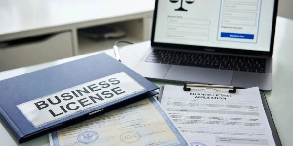 A business license folder and application on a desk with a laptop.