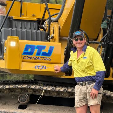 Man smiling next to yellow construction vehicle with DTJ Contracting logo.