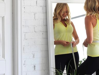 A woman measuring her waist while looking in the mirror and smiling about her weight loss results