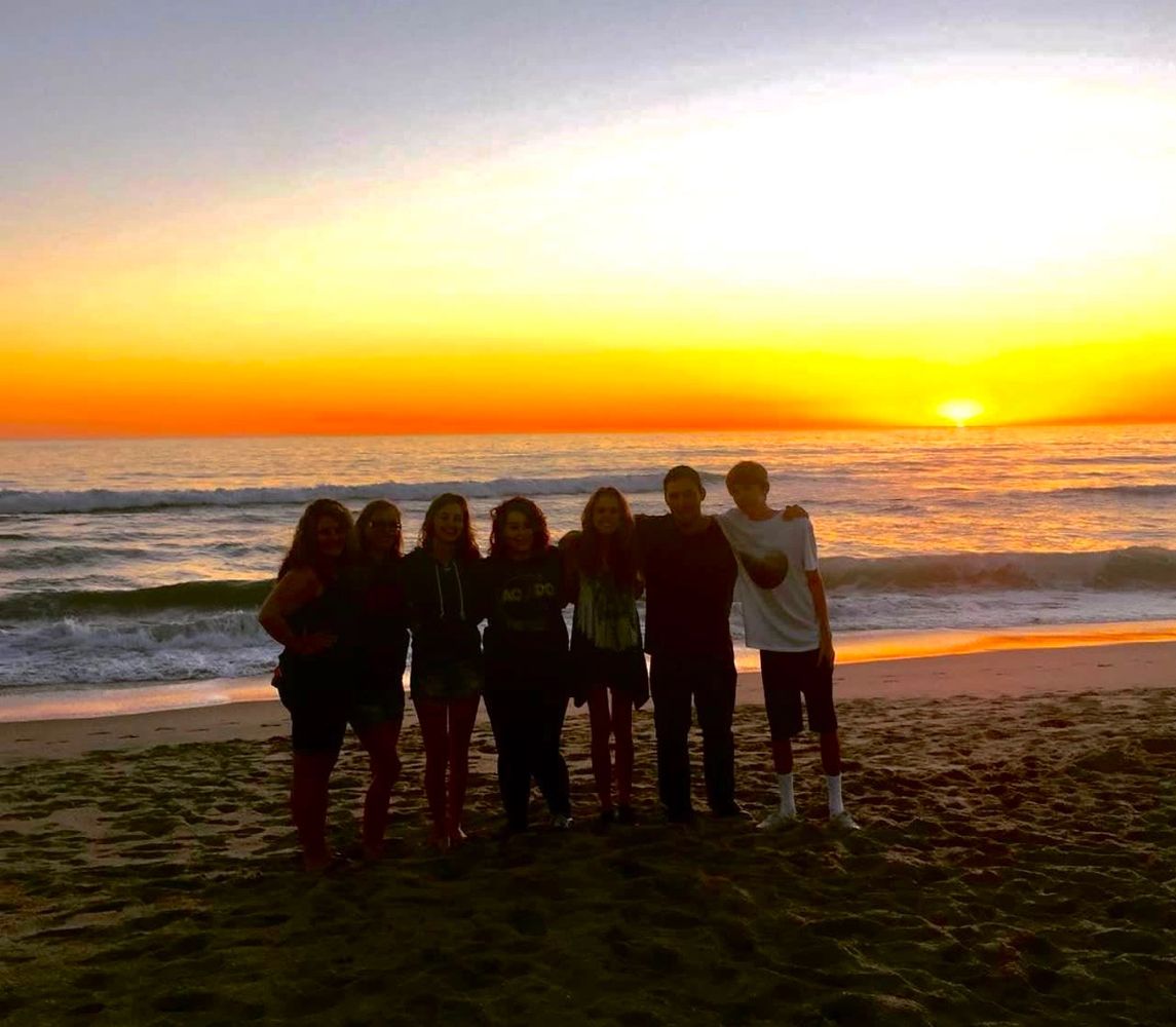 Group of friends silhouetted on the beach at sunset.
