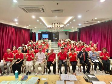 Large group in red shirts posing in a conference room with red curtains.