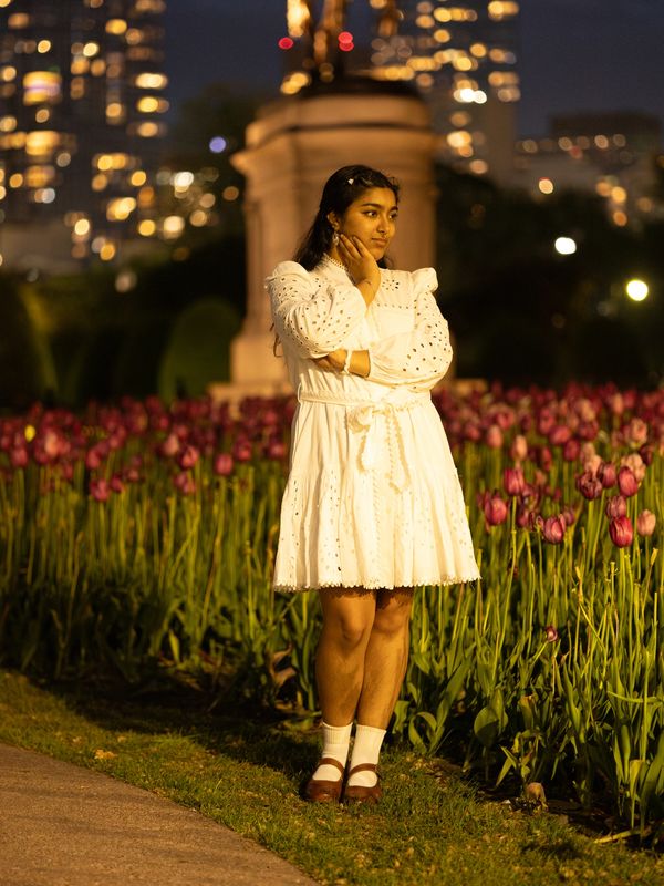 Woman in white dress standing by tulips at night.